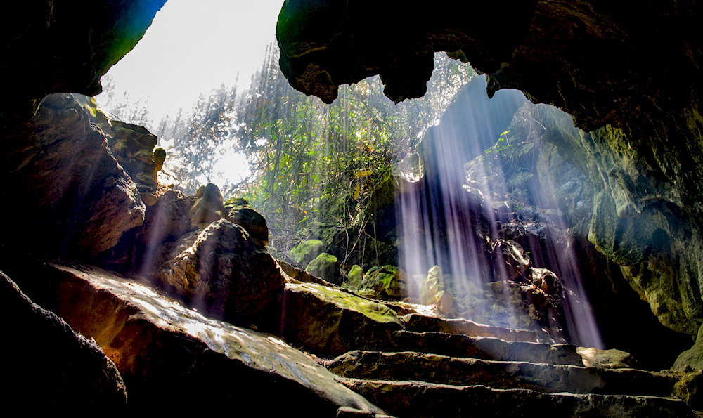 Light filtering through the cave entrance creates a shimmering celestial Milky Way underground 